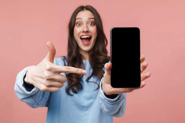Image of attractive young woman with long brown hair smiling and holding cellphone isolated over pink background - Φωτογραφία, εικόνα