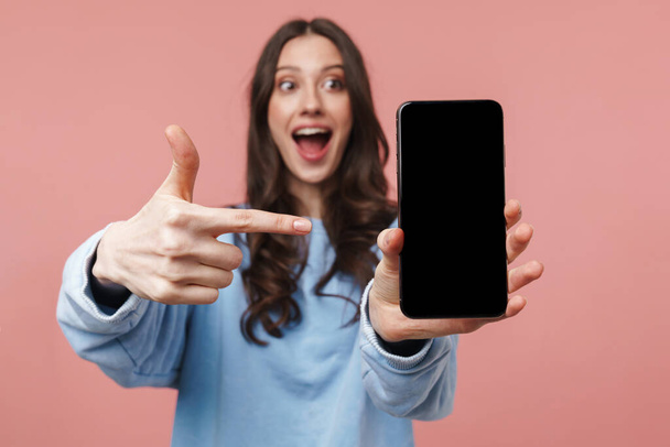 Imagen de una atractiva joven con el pelo largo y castaño sonriendo y sosteniendo el teléfono celular aislado sobre fondo rosa
 - Foto, Imagen