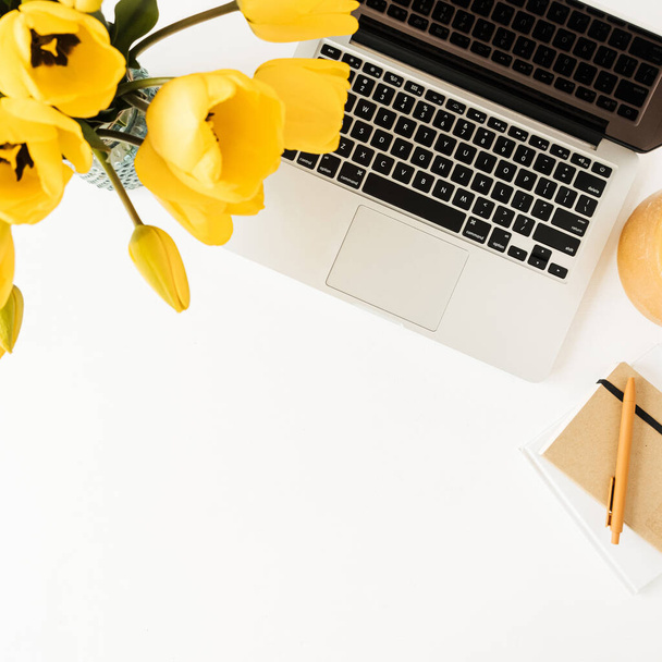 Home Office-Arbeitsplatz mit Laptop, gelbem Tulpenblumenstrauß, Schreibwaren auf weißem Hintergrund. Flache Verlegung, Arbeit von oben, Geschäftskonzept - Foto, Bild