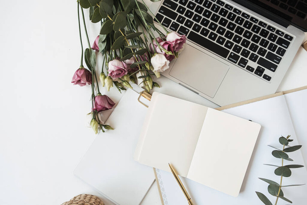 Flat lay lady boss home office workspace with blank paper sheet notebook, laptop, roses flowers bouquet, eucalyptus branch on white table. Top view work at home freelance, outsourcing concept. - Photo, Image