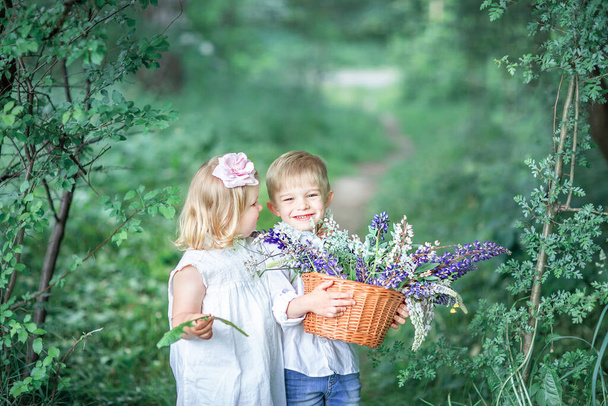 Una niña con un vestido blanco abraza a un niño que sostiene una canasta de flores. Interacción de los niños
 - Foto, imagen