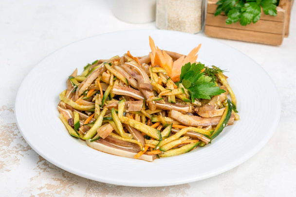 Pork ears salad with vegetables and fresh herbs in a white plate - Фото, изображение