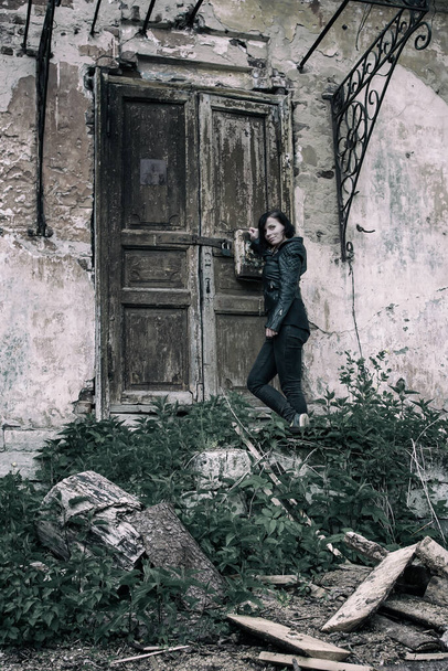 A girl stands near the entrance to an old abandoned house - Φωτογραφία, εικόνα