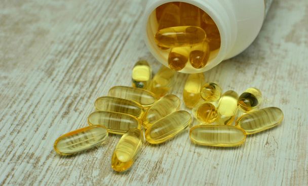 Fish oil capsules with omega 3 and vitamin D in a plastic bottle on a shiny texture with sun beams, healthy diet concept - Photo, Image