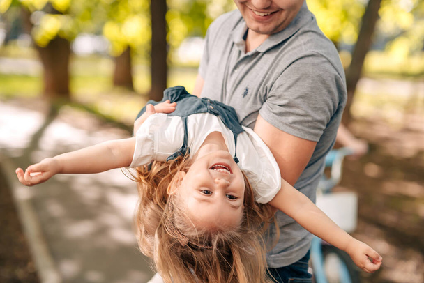  Dad with little daughter play in the park on the street, shakes in his arms, the child laughs, concept happy father's day. Hight quality photo - Foto, Bild