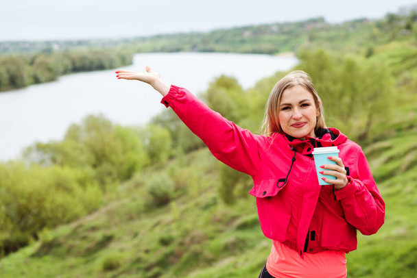 Smiling woman is showing beautiful nature landscape and holding coffee to go cup. - Foto, Bild