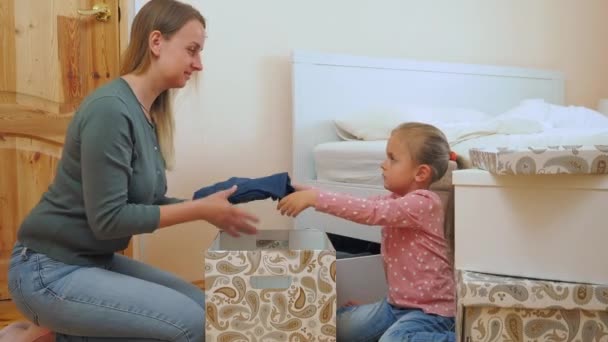 Μητέρα και μικρή κόρη βάζοντας τα ρούχα στο κουτί καρτών μαζί - Πλάνα, βίντεο