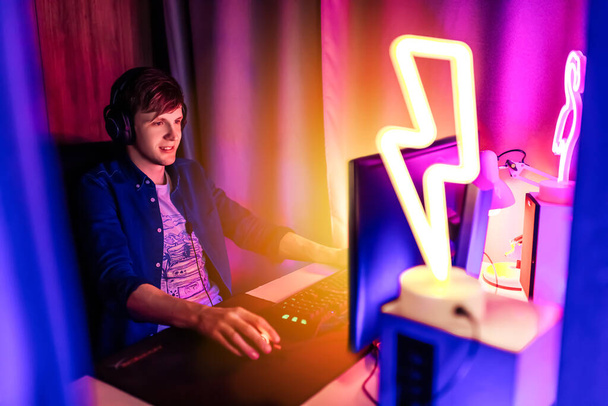 Image of a fun gamer playing video games on a computer with headphones and using a colorful backlit keyboard - Zdjęcie, obraz