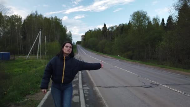 Dívka kráčí po prázdné silnici a snaží se chytit auto stopování - Záběry, video