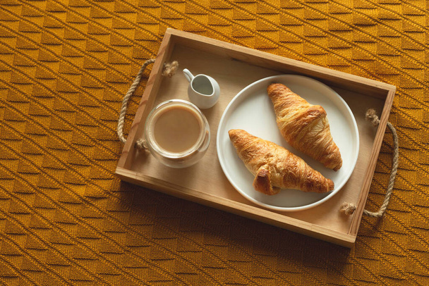 Croissants on a tray with coffee and milkman. Cozy homemade breakfast in bed. Top view. - Photo, Image