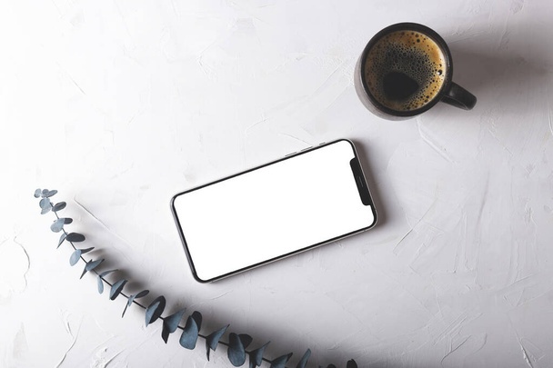 Schermo finto di uno smartphone su un tavolo grigio accanto a un rametto di eucalipto e una tazza di caffè. Schermo isolato
 - Foto, immagini