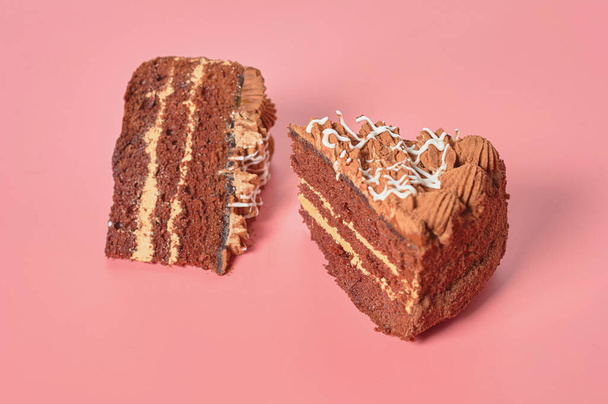 Two pieces of chocolate cake lies on pink table. Close-up - Foto, afbeelding