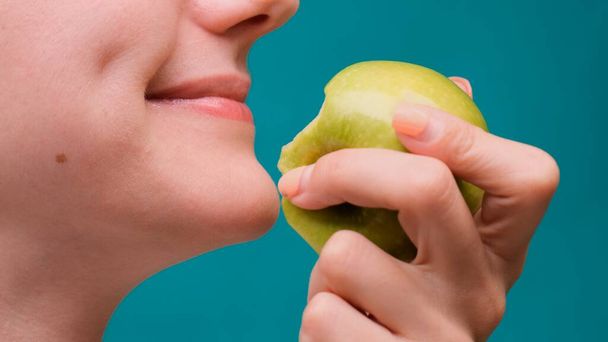 Egészséges táplálkozás és egészséges fogak vagy étrend, fiatal nő harap egy friss alma a zöld képernyőn közelkép - Fotó, kép