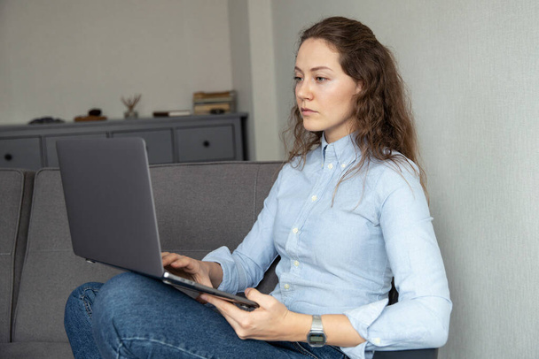 A girl in a shirt and jeans works at a computer at home - Valokuva, kuva