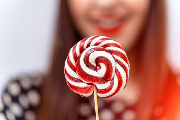 Pretty smiling brunette girl with a lollipop in her hand. Candy on stick. - Foto, afbeelding