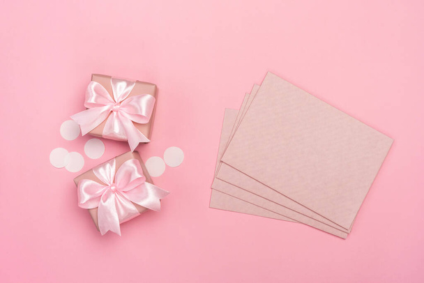 2つのギフトまたはピンクのパステルの背景にコンフェッティと封筒で飾られた箱を提示します。コピースペース付きのトップビュー。誕生日や結婚式のためのフラットレイアウト組成. - 写真・画像