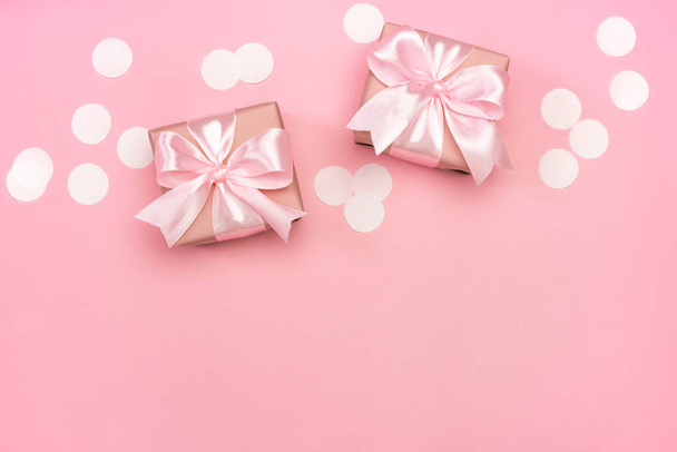 Twee geschenken of geschenkdozen versierd met confetti op roze pastelachtergrond. Bovenaanzicht met kopieerruimte. Platte lay compositie voor verjaardag of bruiloft. - Foto, afbeelding
