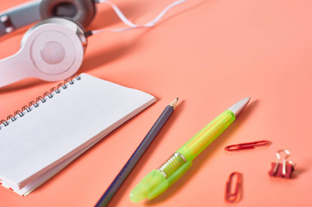 Modern white headphones with cable near blank paper notebook and other stationery things on orange background. Business or school concept. Copy space - Φωτογραφία, εικόνα