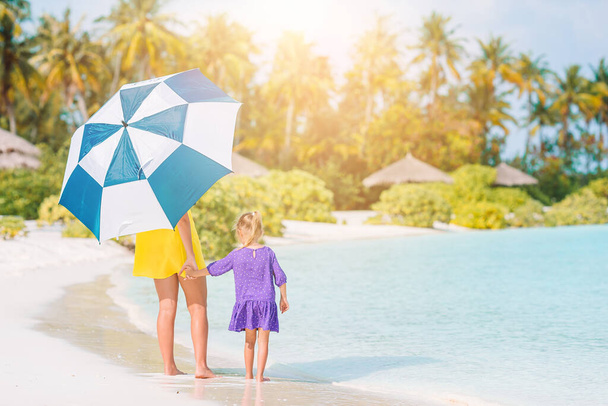 Mladý maminka a jeho dcera kráčející pod deštníkem na bílý písek pláž - Fotografie, Obrázek