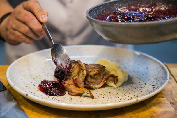 Мясо медальоны в беконе с брокколи и вишни на легкой тарелке красиво консервированы
 - Фото, изображение