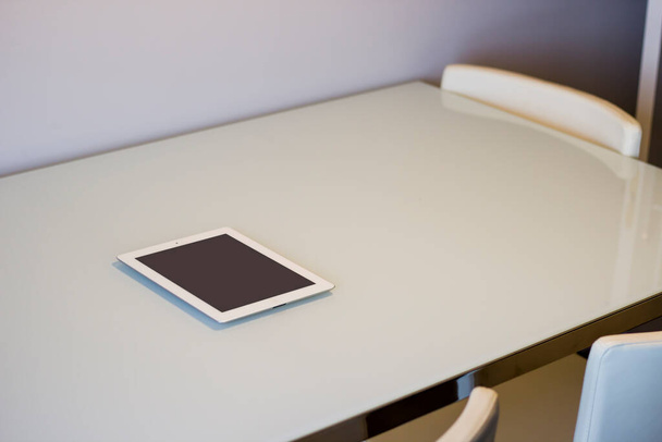 Tableta blanca con pantalla negra en la mesa y sillas alrededor en una sala de estar
. - Foto, Imagen