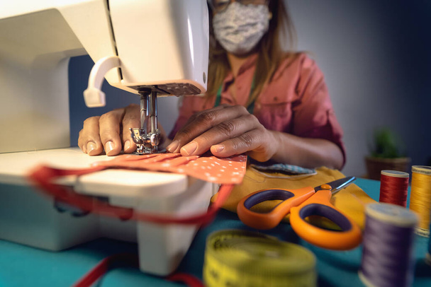 Close up Latijnse vrouwelijke handen naaien met naaimachine zelfgemaakt medisch gezichtsmasker voor het voorkomen en stoppen van verspreiding van corona virus - textielindustrie en covid19 gezondheidszorg concept - Foto, afbeelding