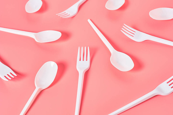 White disposable spoons and forks scattered on pink background. Concept of save environment, ecology, recreation on picnic, party and other events - Valokuva, kuva
