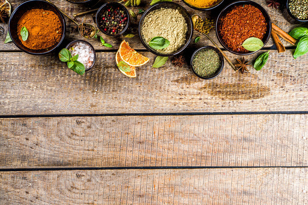 Set of Spices and herbs for cooking. Small bowls with colorful  seasonings and spices - basil, pepper, saffron, salt, paprika, turmeric. On rustic wooden plank table background, top view copy space - Photo, Image