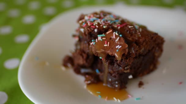 Ein quadratisches Stück Schokoladen-Brownie auf einem Teller, bestreut mit buntem Zuckerpulver. - Filmmaterial, Video