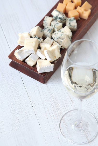 Botella de vino blanco, una copa y queso sobre una tabla de madera
 - Foto, Imagen