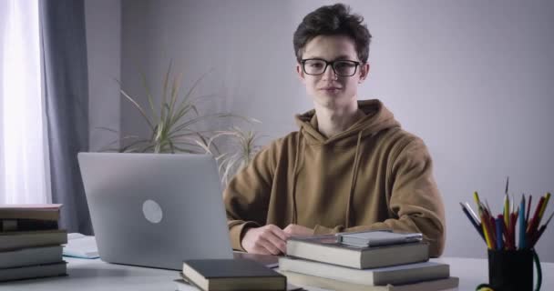 Smart Caucasian boy showing thumb up and smiling at camera. Portrait of intelligent male college student posing at home as doing homework. Education, lifestyle, intelligence. Cinema 4k ProRes HQ. - Záběry, video