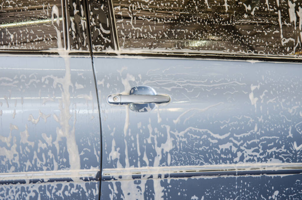 Μπλε αυτοκίνητο, πλύνετε το αυτοκίνητο με φυσαλίδες αφρού στο πλυντήριο αυτοκινήτων. - Φωτογραφία, εικόνα
