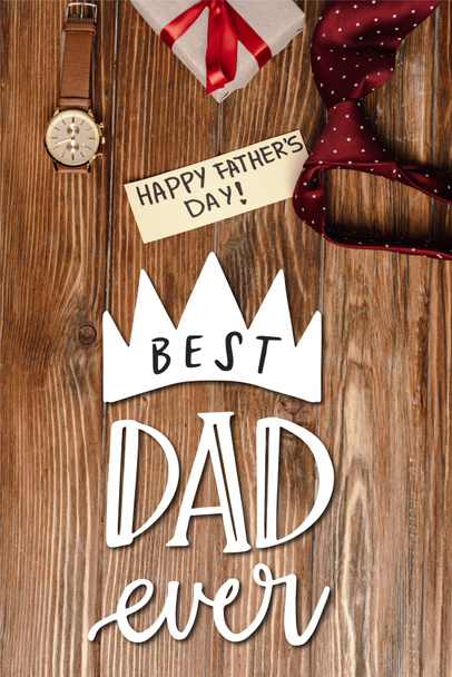 Top view of gift box with red bow, greeting card with lettering happy fathers day and mens red tie and wristwatch on wooden background, best dad ever illustration - Photo, Image