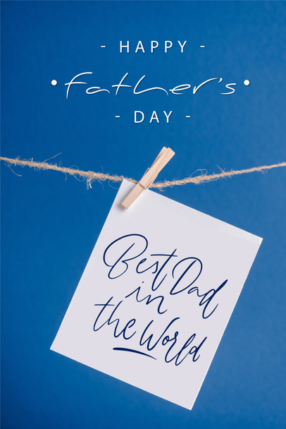 Tarjeta de felicitación blanca con mejor papá en el mundo ilustración colgando de la cuerda con pinzas de ropa aisladas en azul
 - Foto, imagen