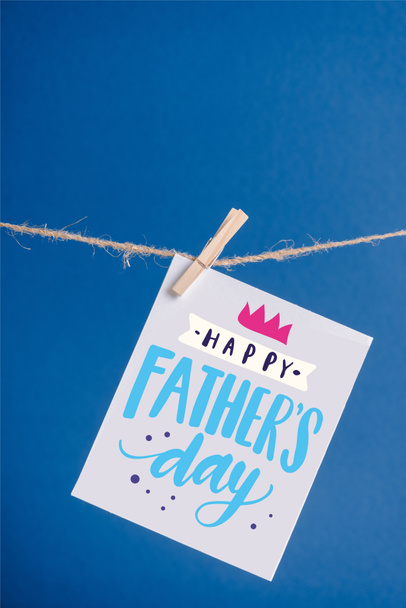 White greeting card with happy fathers day illustration hanging on rope with clothespins isolated on blue - Fotó, kép