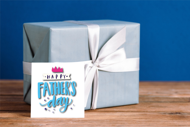 selective focus of greeting card with happy fathers day illustration and gift box with white bow isolated on blue - Photo, Image