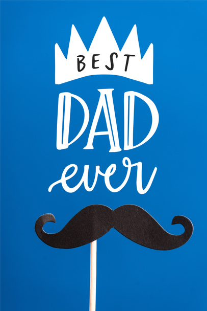 Papel preto decorativo crafted bigode falso no pau branco isolado em azul, melhor pai já ilustração
 - Foto, Imagem