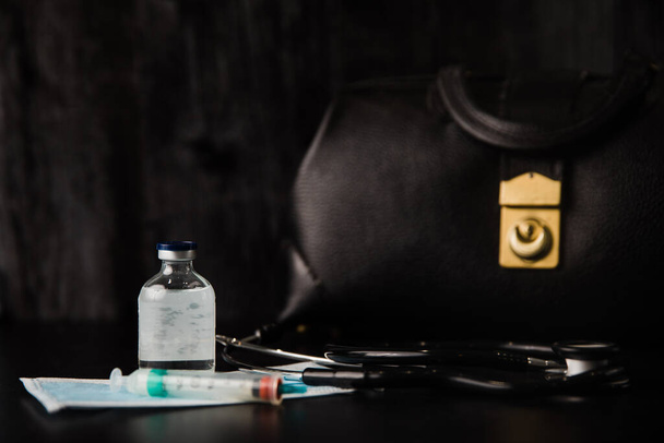 Gezondheidszorg zwarte vintage dokters medische tas met een stethoscoop voor een arts om te gebruiken op het werk of thuis gesprekken met stethoscoop, geneeskunde, beschermende gezichtsmasker en een spuit - Foto, afbeelding