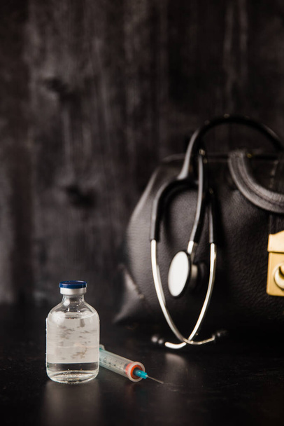 Gezondheidszorg zwarte vintage dokters medische tas met een stethoscoop voor een arts om te gebruiken op het werk of thuis gesprekken met stethoscoop, medicijnen en een spuit - Foto, afbeelding