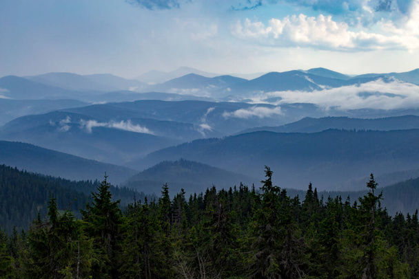 Güneşin ışınlarıyla aydınlanan puslu dağlar bulutlu gökyüzünden kırılıyor.. - Fotoğraf, Görsel