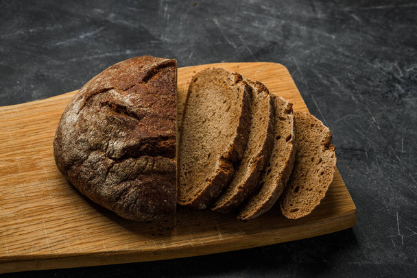 Rustic bread and slices on dark background. Handmade cutting board. - Фото, зображення