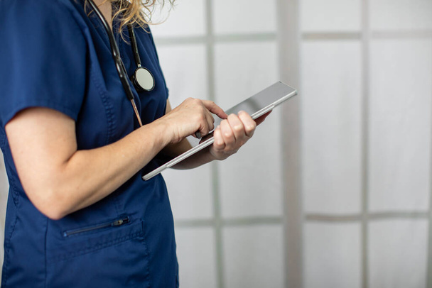 Una profesional médica femenina que usa exfoliantes con tecnología escribiendo notas de pacientes en una tableta
 - Foto, Imagen