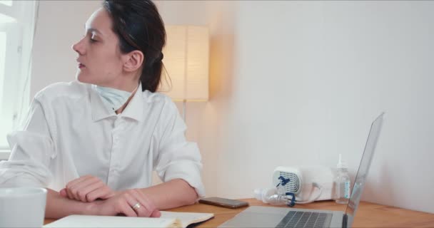 Beautiful young doctor woman feeling sick working from home consulting patients using laptop on COVID-19 lockdown. - Video