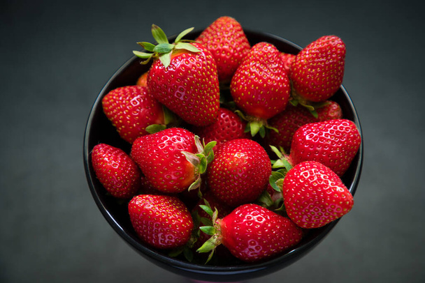 Fresh ripe strawberries in a black bowl isolated on neutral background, top view. - Foto, afbeelding