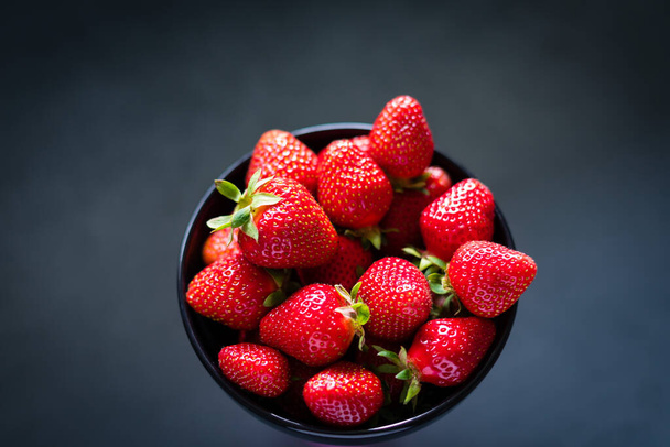 Fresh ripe strawberries in a black bowl isolated on neutral background, top view. - Фото, изображение