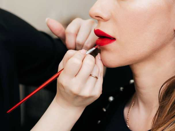 maquillaje artista pone lápiz labial rojo con cepillo en los labios de una mujer
 - Foto, Imagen