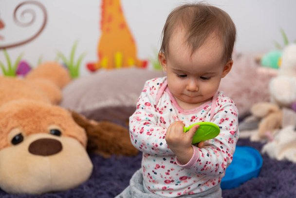 Солодкий 1 річний портрет дівчинки з гумовою жувальною іграшкою в її світлій кімнаті
 - Фото, зображення