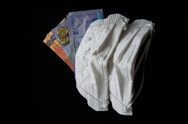 Λεφτά από το Καζακστάν και μια αντιική μάσκα. Το Καζακστάν κρατάει χαρτονομίσματα και κέρματα κατά τη διάρκεια πανδημίας. Κορονοϊός στο Καζακστάν και χρήματα. Τεντζ και κορωνοϊός. Οικονομία του Καζακστάν και COVID 19. Καζαχστάν - Φωτογραφία, εικόνα