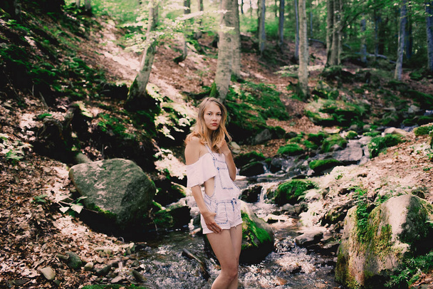 Happy tourist girl teenager in forest near to the cold fresh stream river at the waterfall Shypit, cascade in Pylypets in the forest. Carpathian Mountains. Ukraine. summer festival - 写真・画像