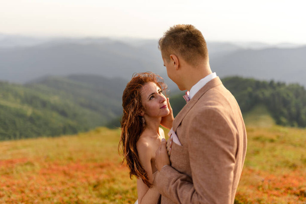 Gli sposi si abbracciano teneramente. Tramonto. Foto di matrimonio su uno sfondo di montagne di autunno. Un forte vento gonfia capelli e vestiti. Primo piano
. - Foto, immagini